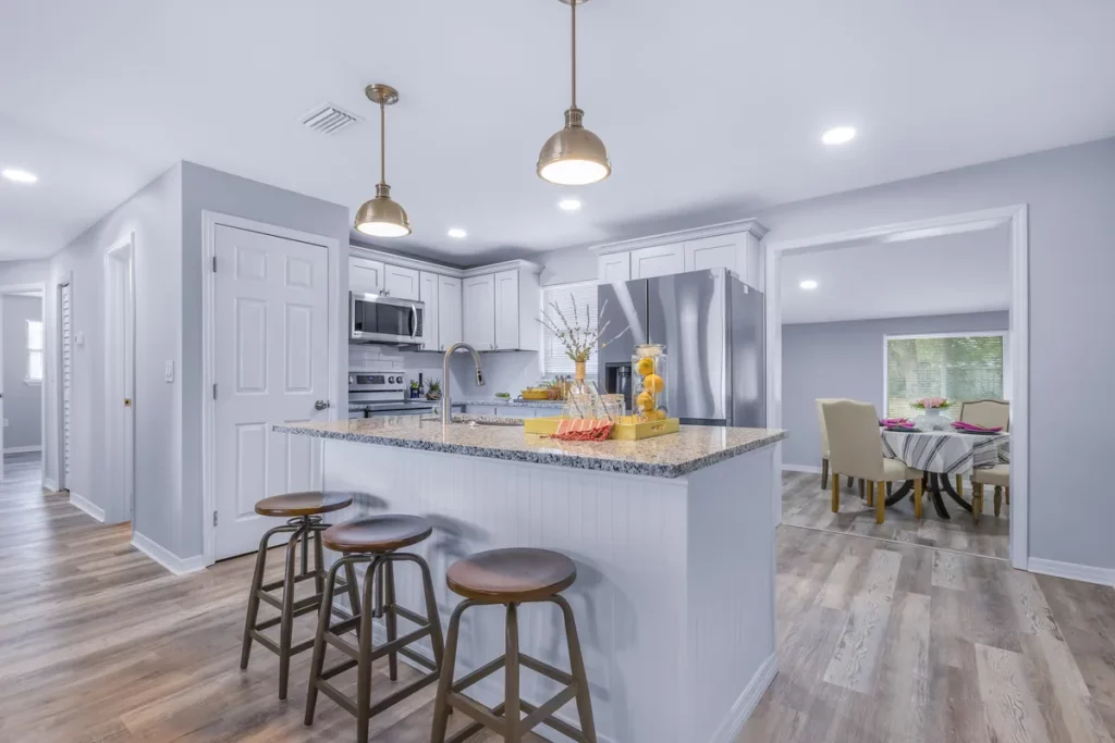Jacksonville, FL kitchen with white cabinets, granite island, stainless steel appliances, and three bar stools