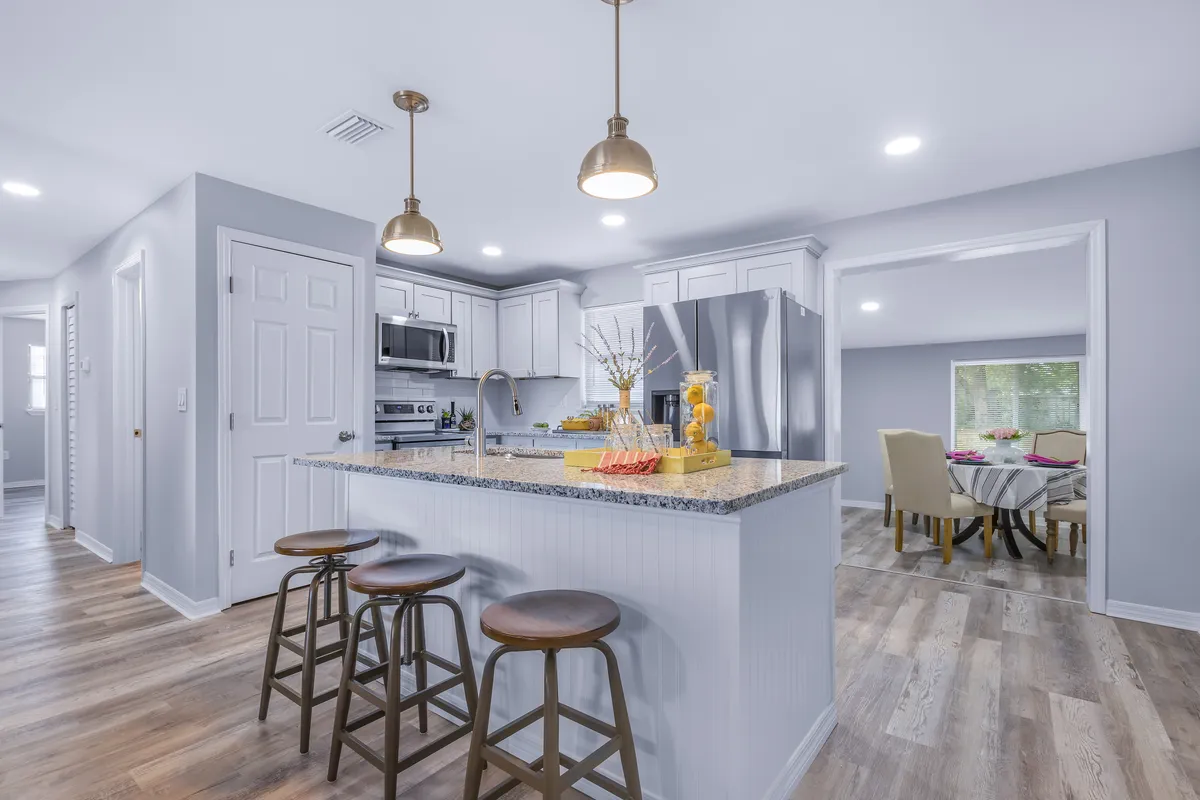 Jacksonville, FL kitchen with white cabinets, granite island, stainless steel appliances, and three bar stools