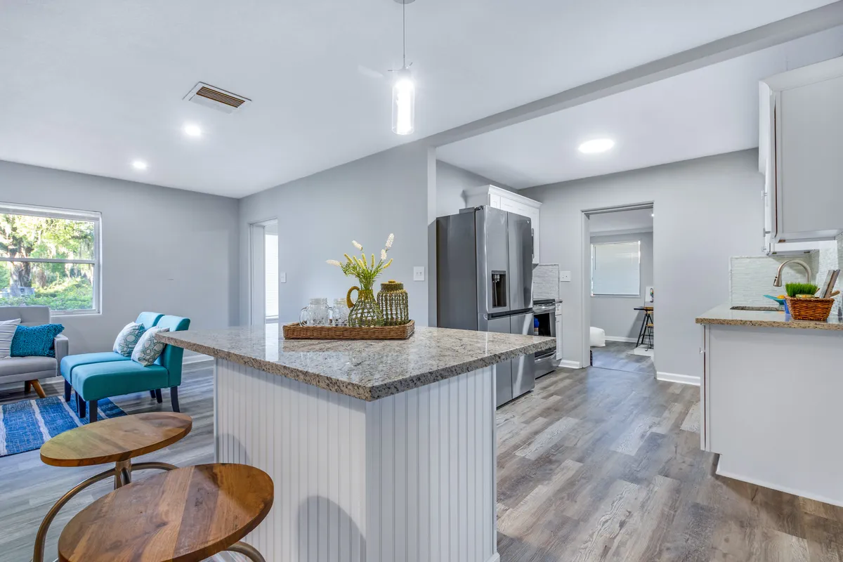 Open kitchen in Jacksonville, FL with granite peninsula, white cabinetry, stainless steel refrigerator, and wood-look flooring