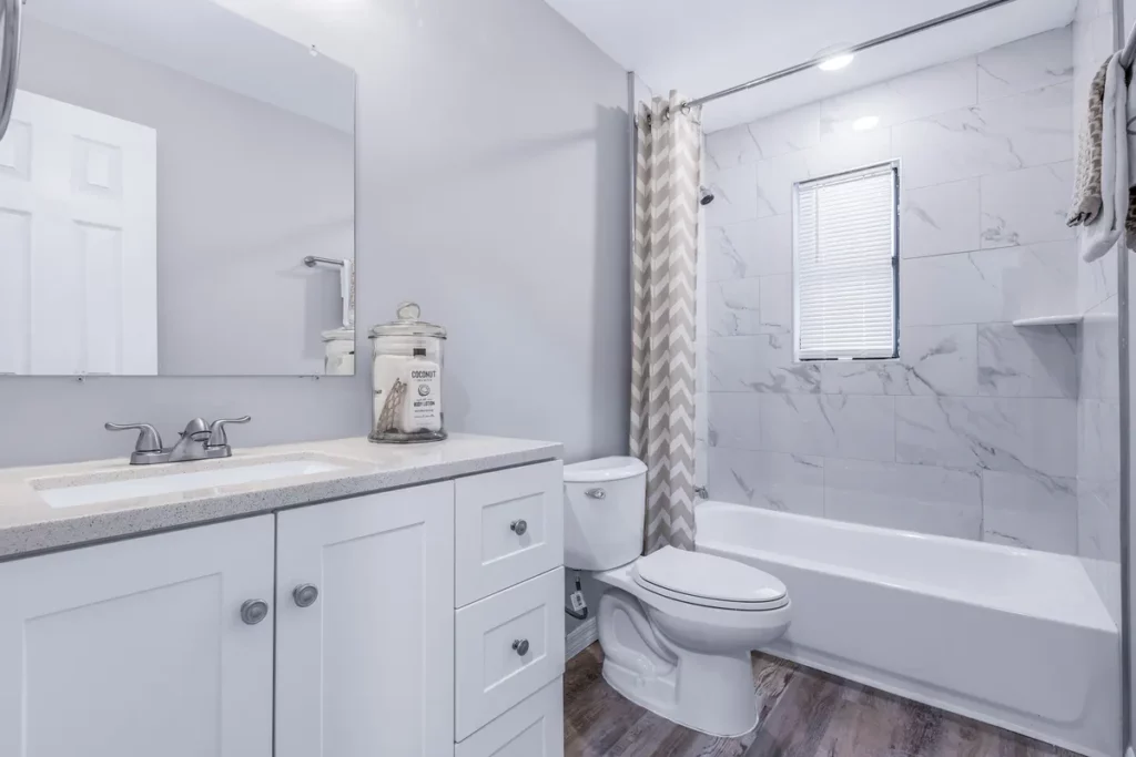 Bathroom with white vanity, large mirror, bathtub, marble-look wall tile, and wood-look flooring in Jacksonville, FL