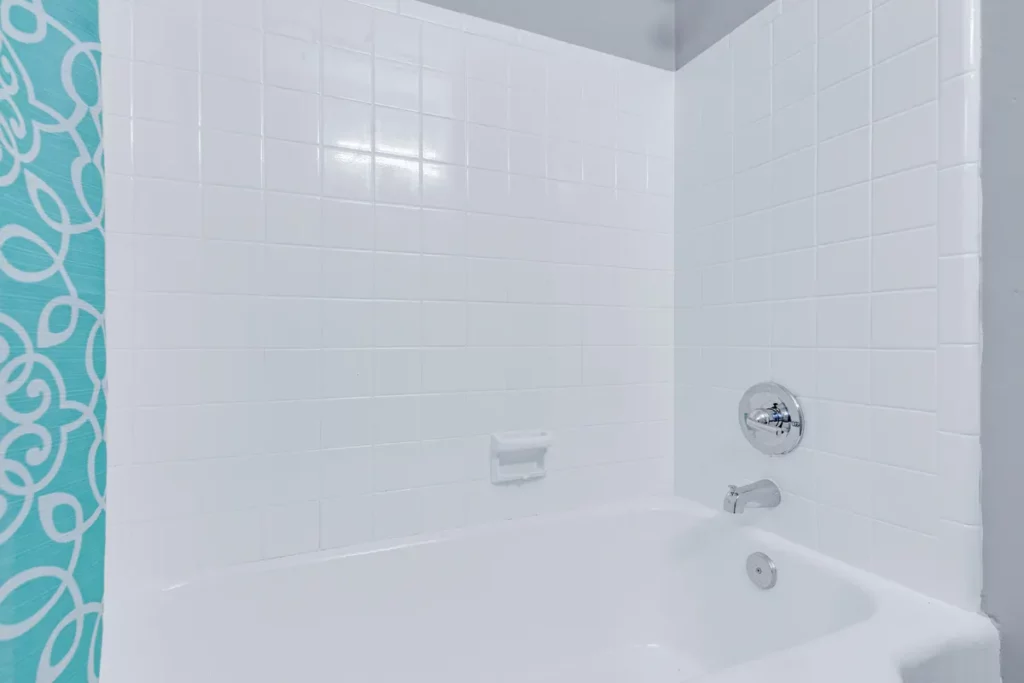 Bathtub with white square wall tile, chrome fixtures, built-in soap dish, and turquoise patterned shower curtain in Jacksonville, FL
