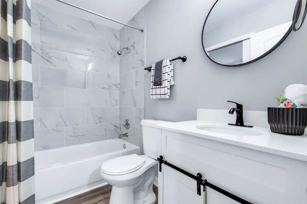 Bathroom with white vanity, black faucet, bathtub, marble-look wall tile, and striped shower curtain in Jacksonville, FL
