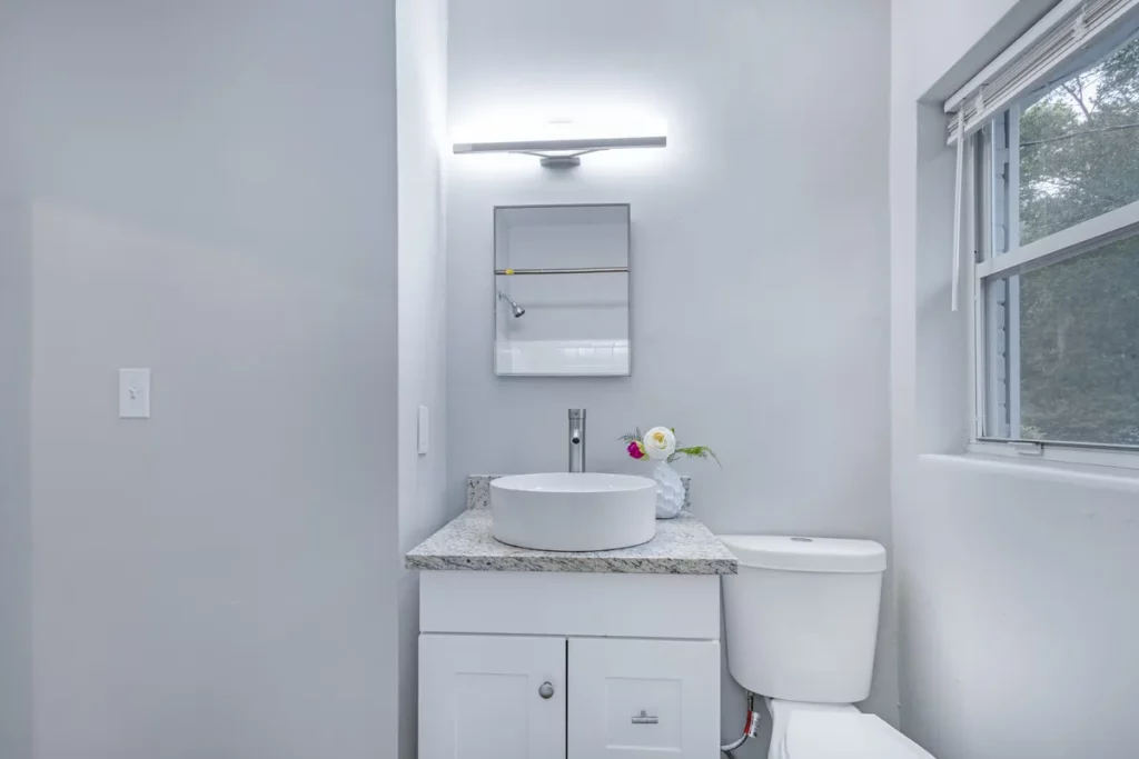 Bathroom with white vanity, round vessel sink, granite countertop, wall mirror, toilet, and window in Jacksonville, FL