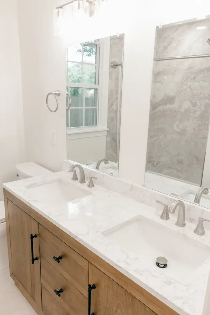Two rectangular undermount sinks set in a white marble-look vanity top with light wood cabinetry, black drawer pulls, nickel faucets, and two tall mirrors in Jacksonville, FL.