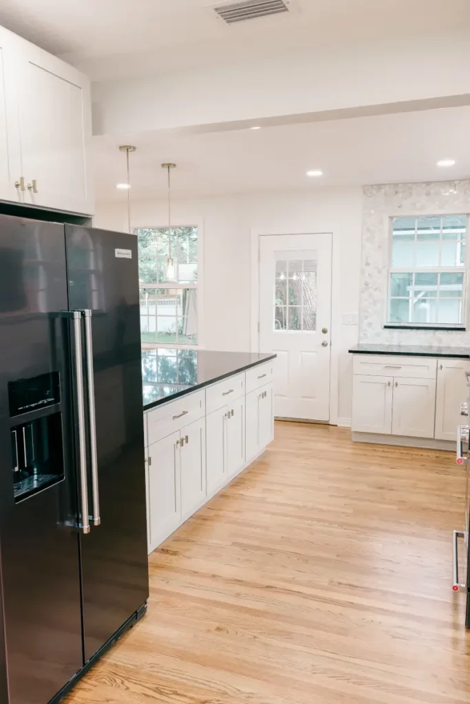 Kitchen with a black side-by-side refrigerator, white shaker cabinets, black countertops, hardwood flooring, and exterior door.