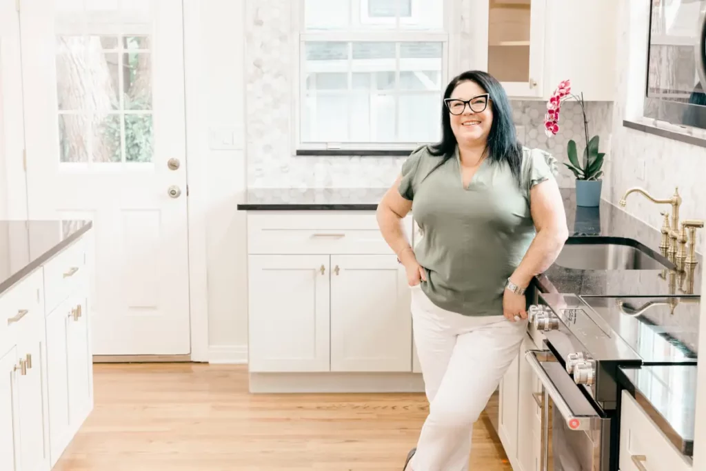 Ingrid Silvan standing in a kitchen she designed with white cabinets, dark countertops, and gold hardware in Jacksonville, FL