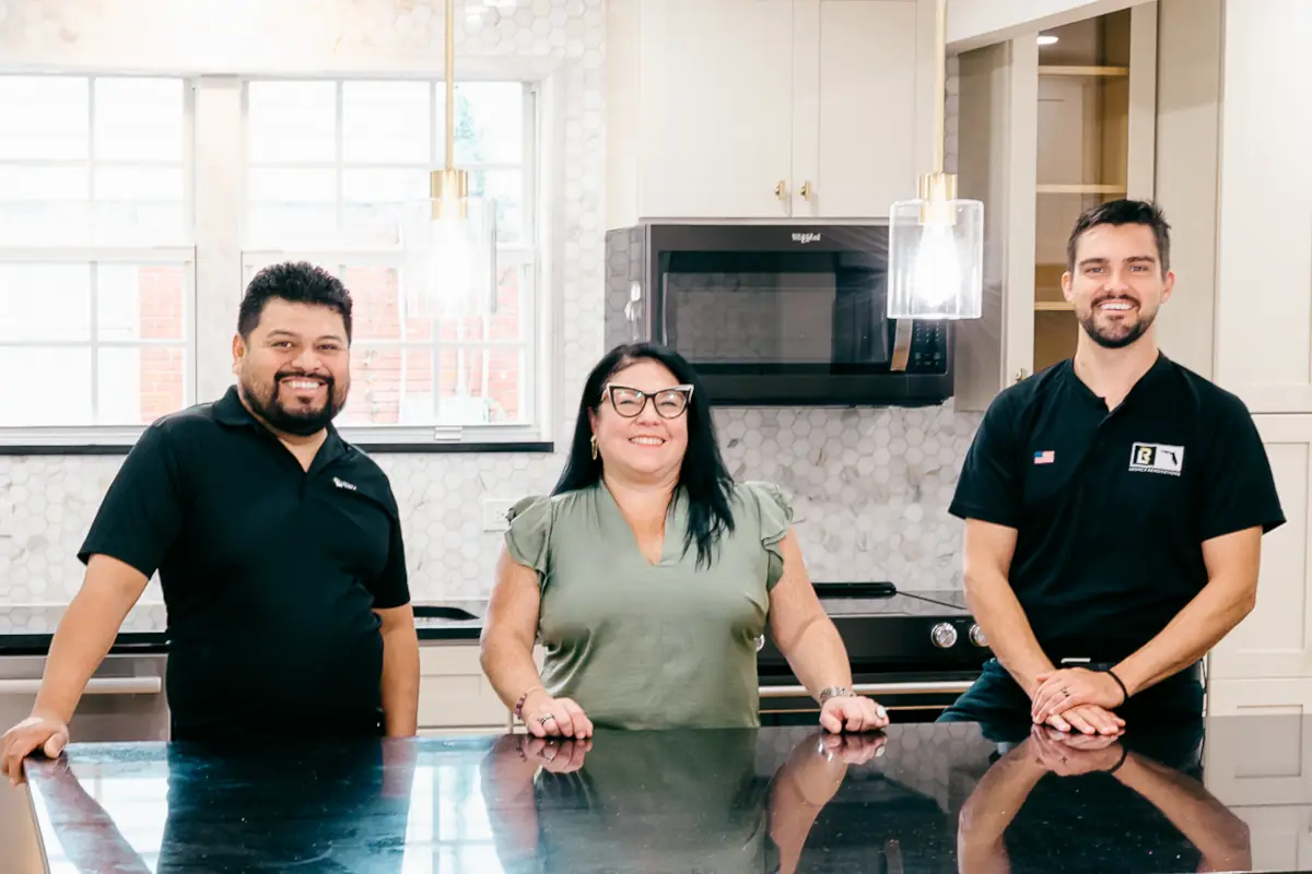 Three members of the Legacy Renovations team posing behind a black island countertop inside a kitchen in Jacksonville, FL.