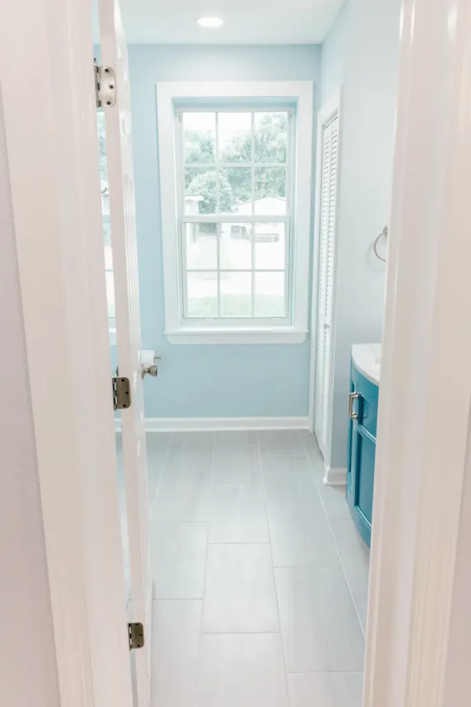 Bathroom with light blue walls, gray tile flooring, white trim, window, and blue vanity in Jacksonville, FL.
