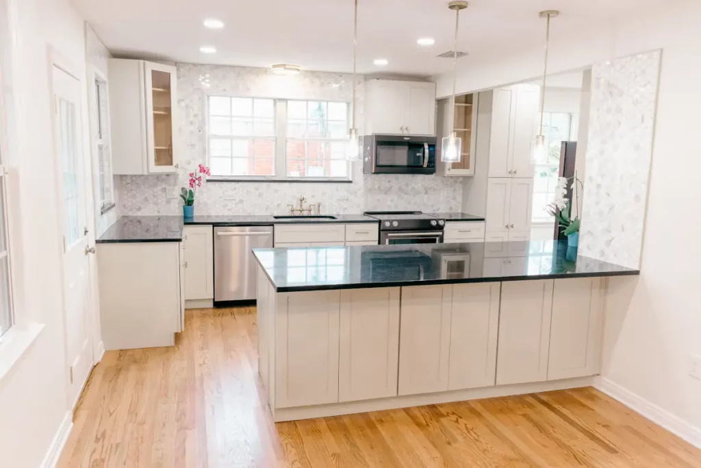 Kitchen with white cabinets, black countertops, stainless steel appliances, hardwood flooring, and a large center island.