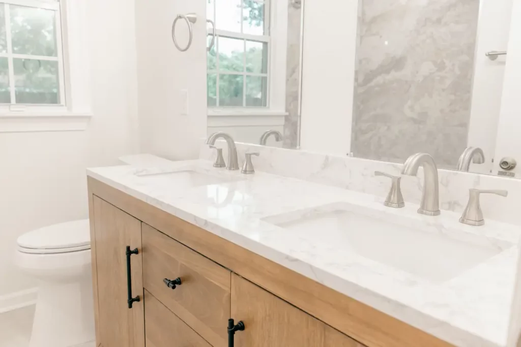 Wood bathroom vanity with two sinks, marble countertop, large mirror, and windows in Jacksonville, FL