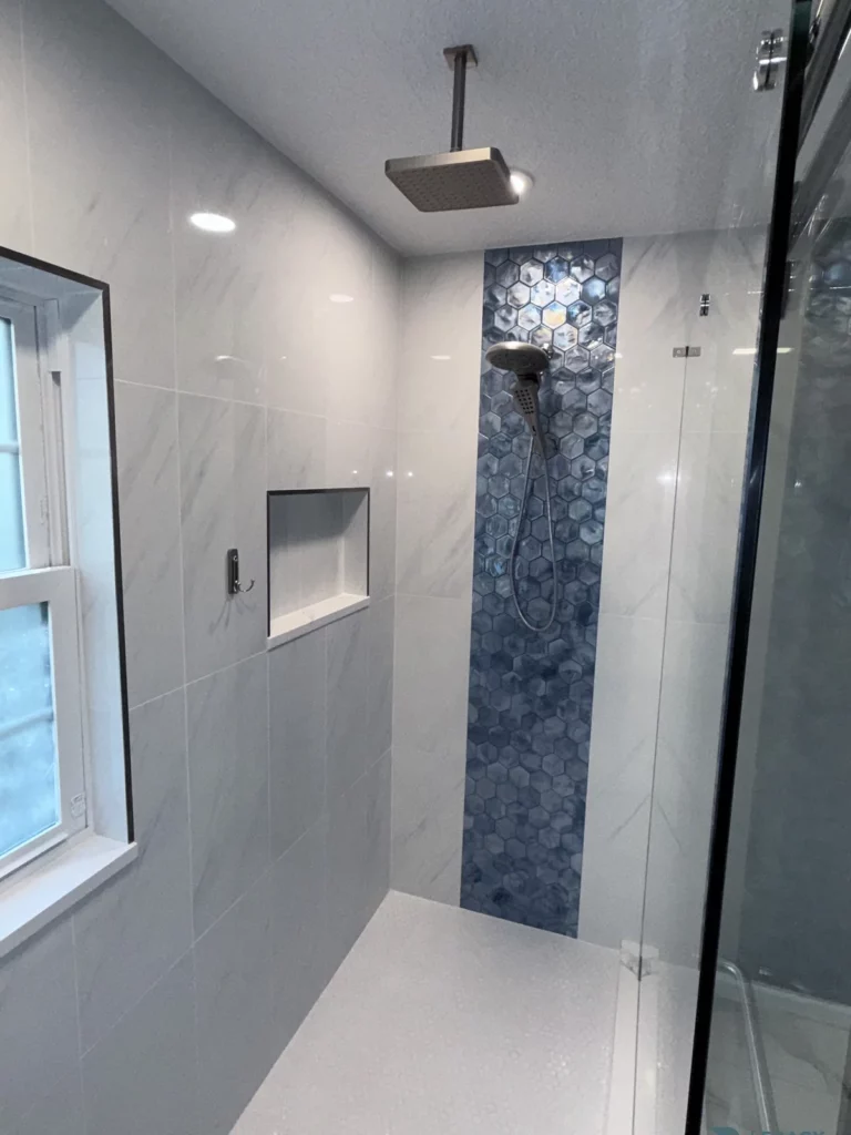 Walk-in shower with a blue hexagon tile center panel, recessed niche, handheld sprayer, overhead showerhead, and window in Jacksonville, FL