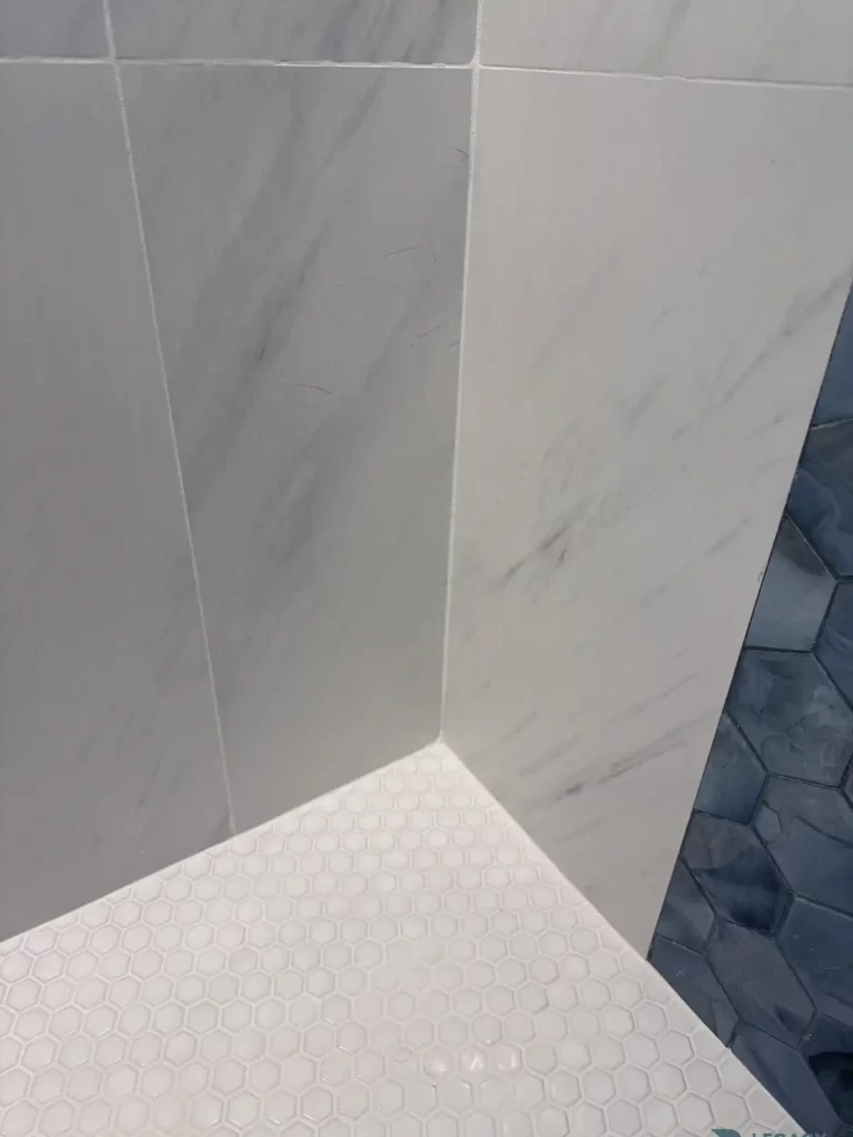 Close-up of large marble-look wall tiles meeting a small white hexagon shower floor and blue accent tile in Jacksonville, FL