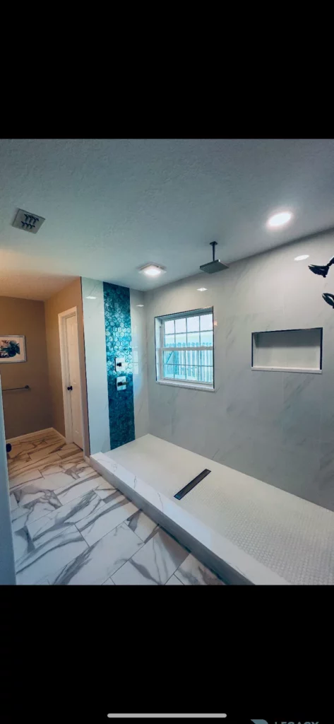 Beach Haven bathroom showing a tiled walk-in shower, blue hexagon accent strip, window, niche, and marble-pattern floor in Jacksonville, FL