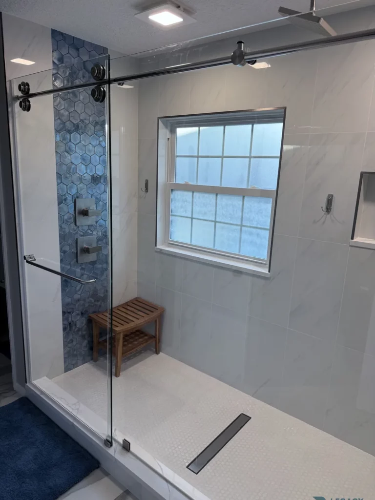 Walk-in shower with blue hexagon accent tile, glass enclosure, window, and wood bench in Beach Haven, Jacksonville, FL
