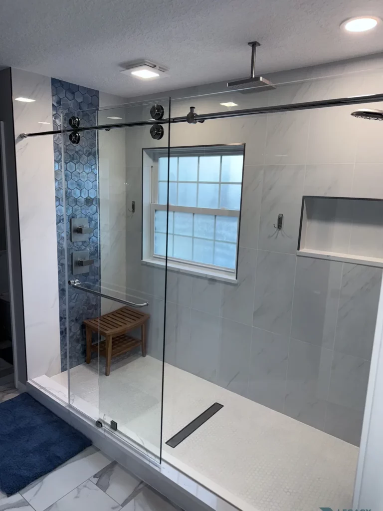 Glass-enclosed walk-in shower with blue hexagon tile, wooden bench, window, recessed niche, and overhead showerhead in Jacksonville, FL