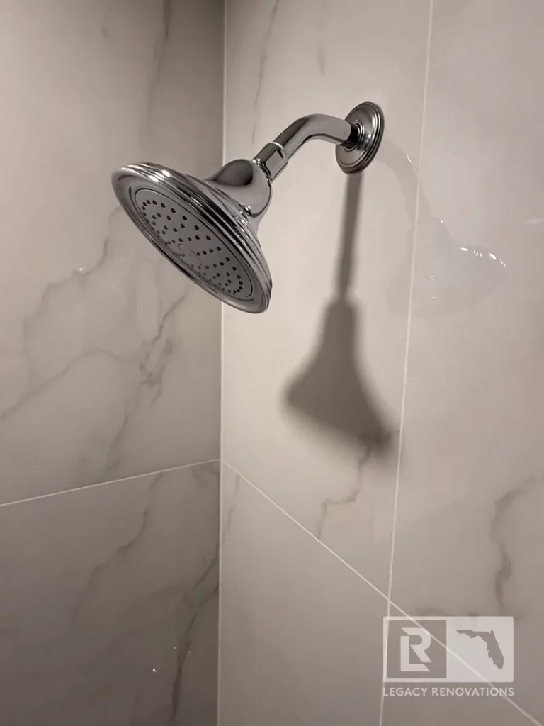 Chrome showerhead mounted on marble-look wall tile in a San Jose bathroom, Jacksonville, FL