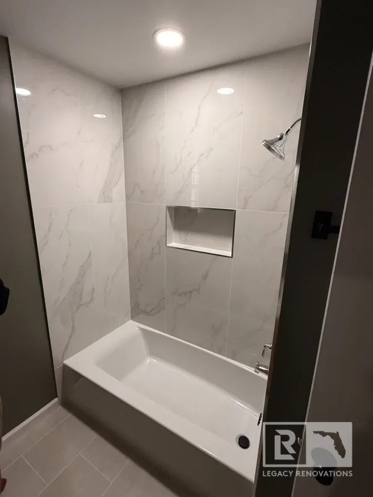 White marble-look shower wall tile with bathtub, recessed niche, and chrome showerhead in San Jose, Jacksonville, FL