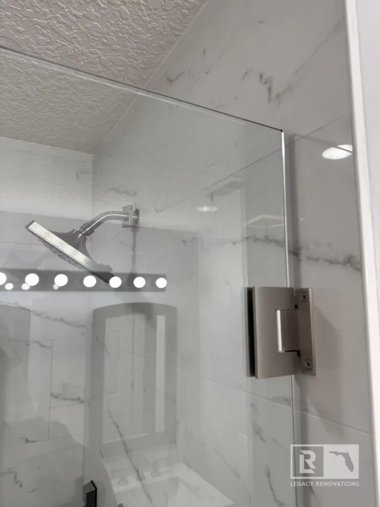 Glass shower door with brushed metal hinge, chrome showerhead, and marble-pattern wall tile in Autumn Green, Jacksonville, FL