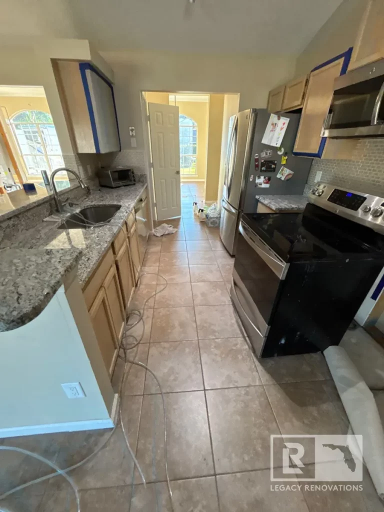Galley kitchen in progress with granite counters, tile floor, tape on cabinets, and stainless appliances on Laura Rose Ct.