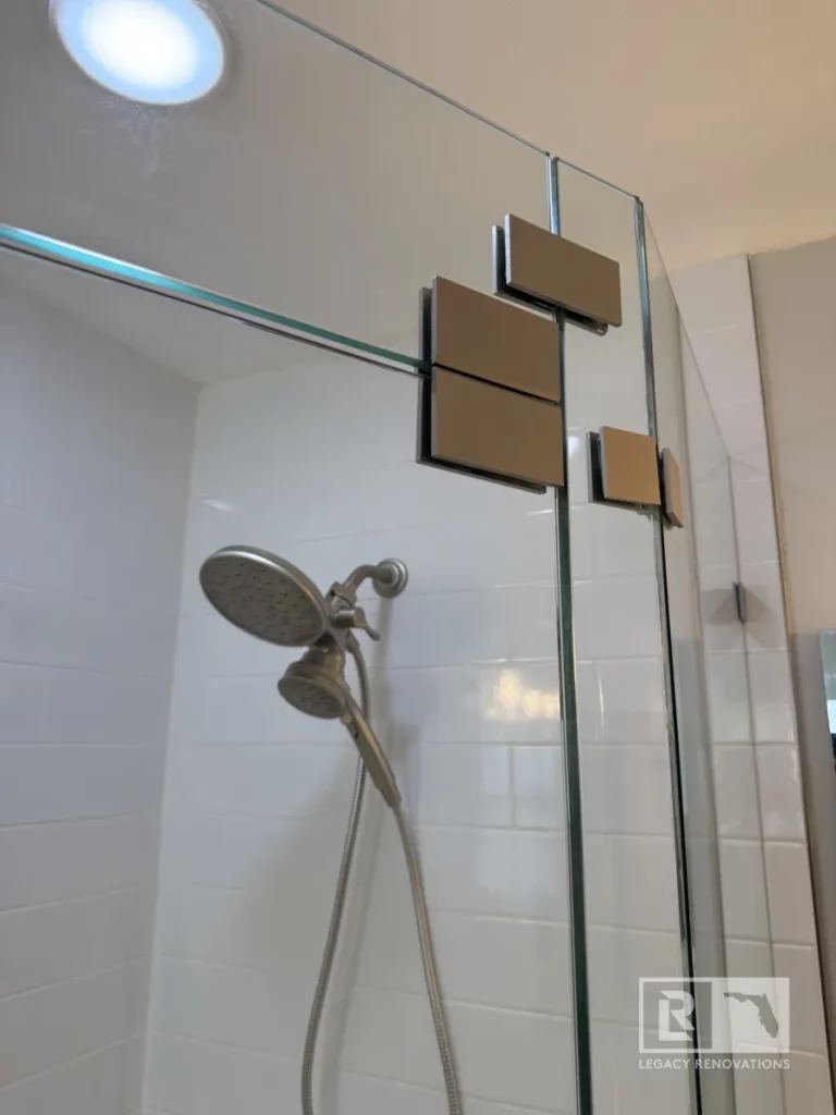 A spacious, corner shower with clear glass shower door, rectangular metal hinges and handheld showerhead in Jacksonville, FL