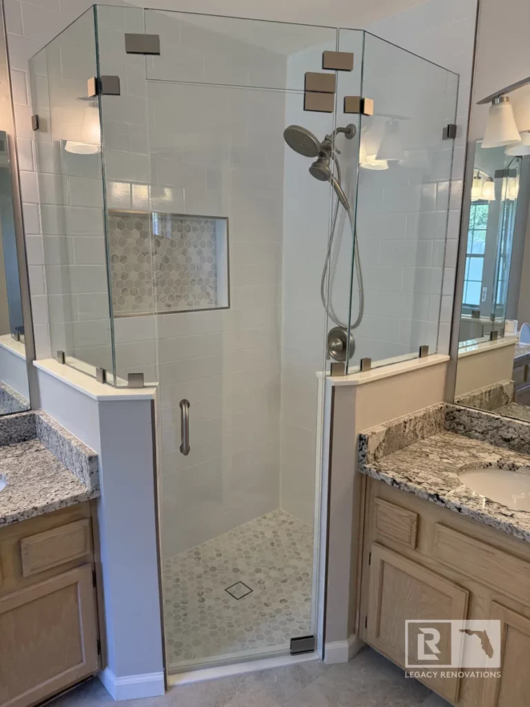 A beautifully remodeled shower featuring a frameless glass enclosure, a handheld showerhead, and a built-in niche with hexagonal tile accents.