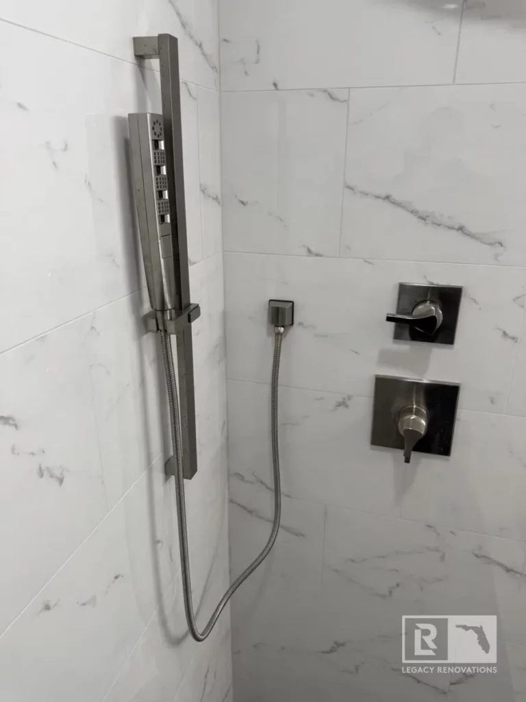 Wall-mounted handheld shower sprayer with two control valves and white marble-look tile in Jacksonville, FL