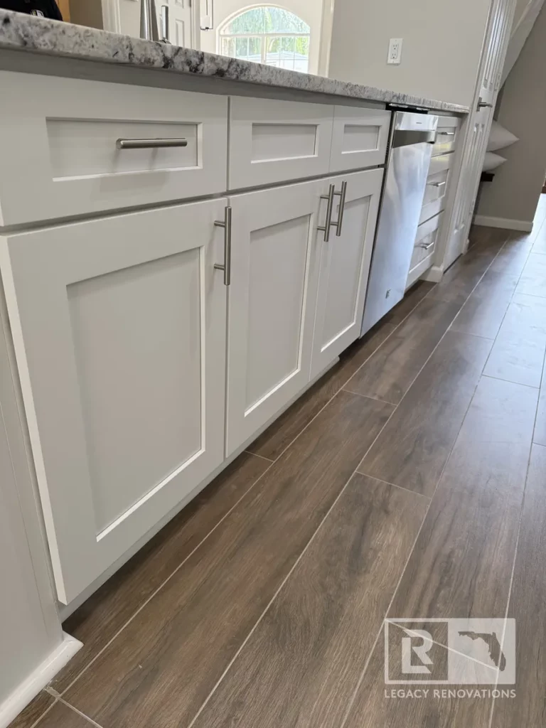 Row of lower white island drawers and cabinet doors next to a stainless dishwasher on wood-plank tile flooring on Laura Rose Ct.