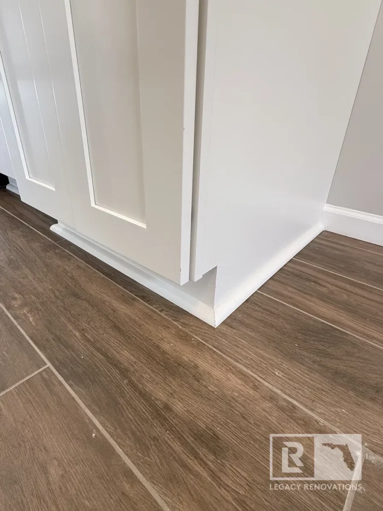 White shaker cabinet corner with toe kick trim and shoe molding set on wood-grain tile floor on Laura Rose Ct.