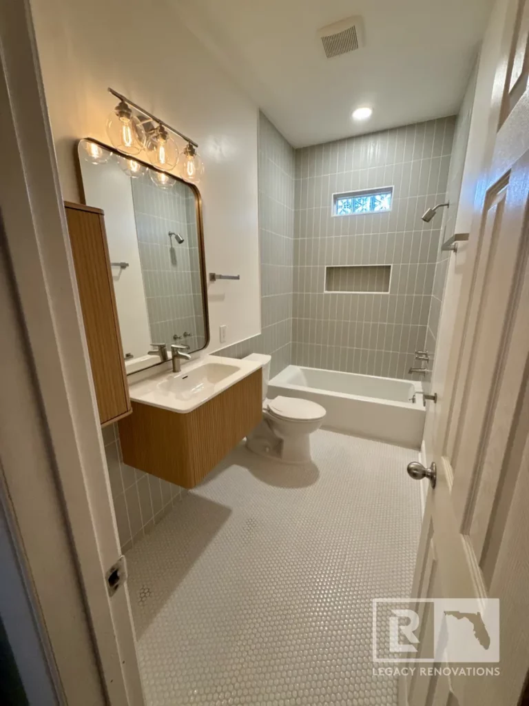 Bathroom viewed from the doorway with a wood vanity, bathtub, tiled walls, recessed niche, and small floor tiles in Jacksonville, FL