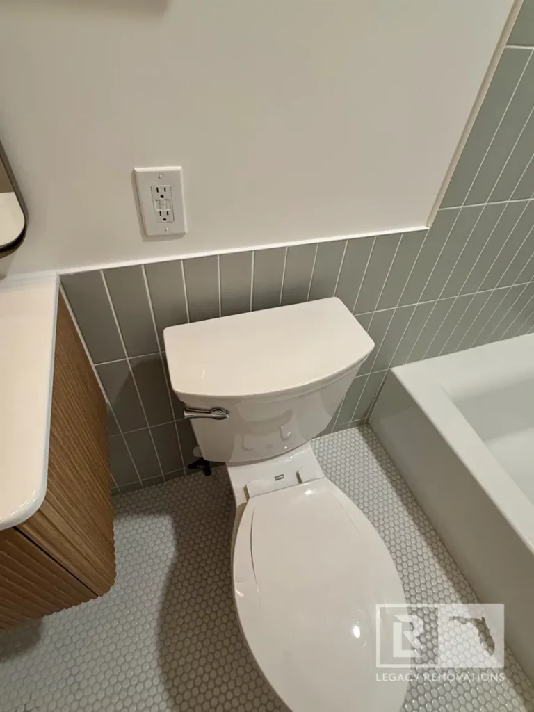 White toilet beside a bathtub with gray wall tile and small round floor tiles in Jacksonville, FL
