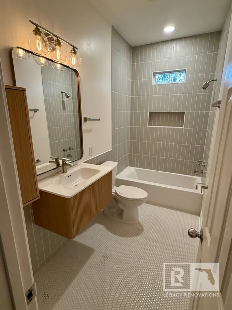 Bathroom viewed from the doorway with a wood vanity, bathtub, recessed wall niche, glass block window, and round floor tiles in Jacksonville, FL