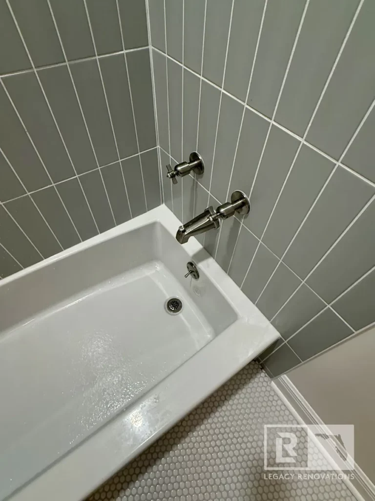 White bathtub with chrome fixtures, gray wall tile, and small round floor tiles in Jacksonville, FL