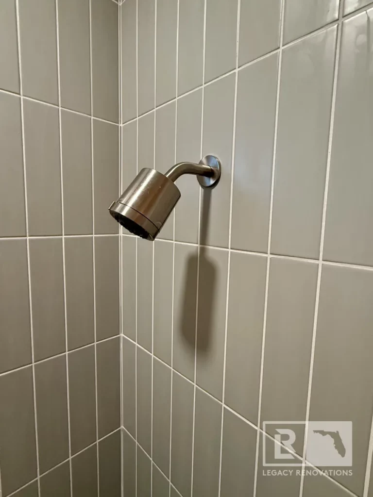 Chrome shower head mounted on a gray tiled wall at the corner of a bathroom in Jacksonville, FL