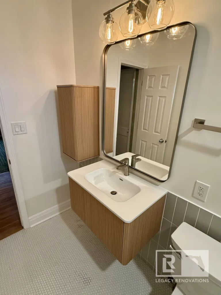 Fluted wood vanity with integrated sink, rounded mirror, four-light fixture, and penny tile floor in Jacksonville, FL