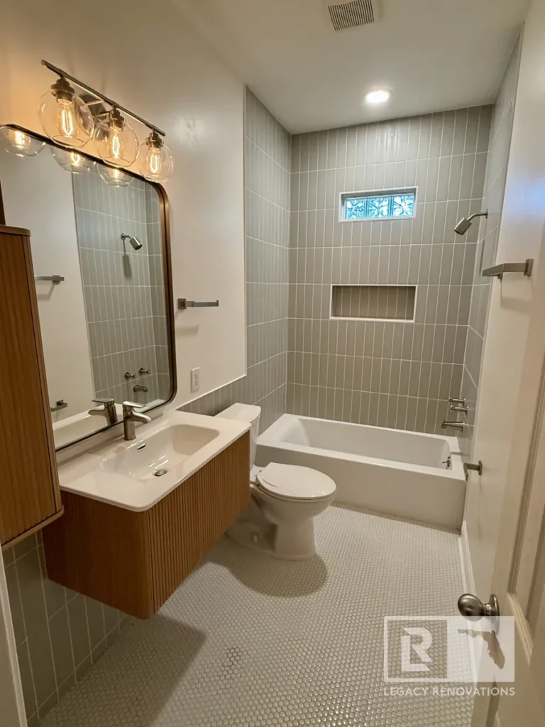 Bathroom with gray wall tile, wood vanity, bathtub, toilet, and round floor tile in Jacksonville, FL