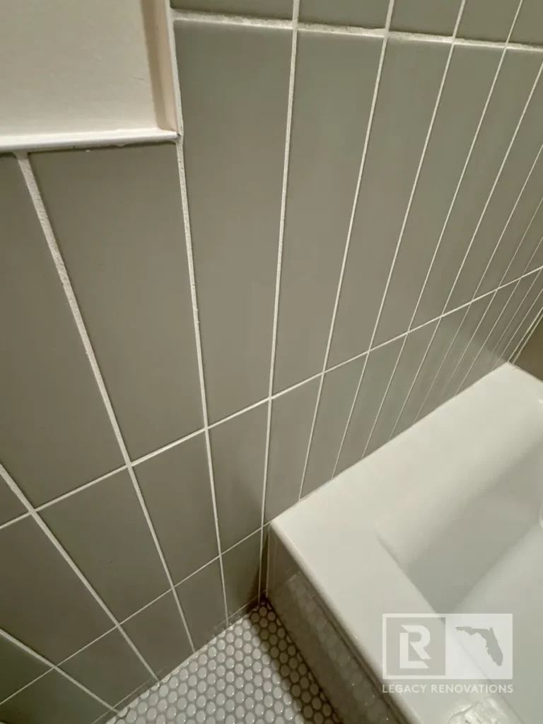 Close-up of gray rectangular wall tile beside a white bathtub and small round floor tiles in Jacksonville, FL