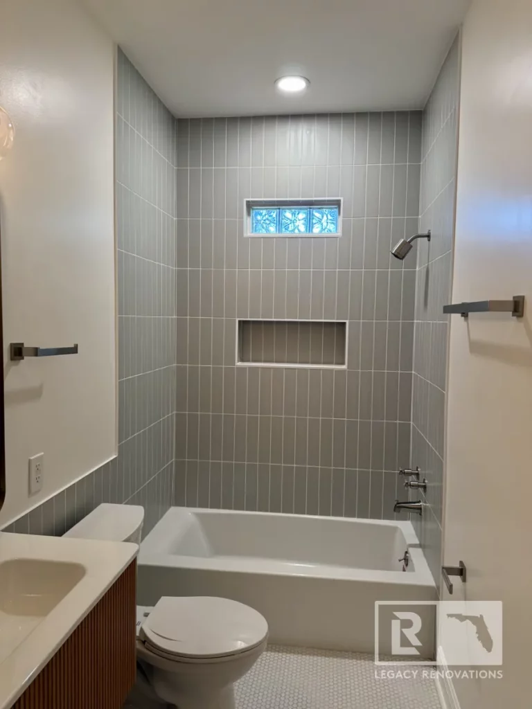 Walk-in shower with white marble-look wall tile, frameless glass enclosure, square rain showerhead, handheld shower, and corner shelves in Jacksonville, FL.