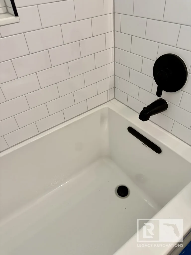 Close-up of a white bathtub with matte black faucet, drain, overflow cover, and white subway tile walls in Jacksonville, FL