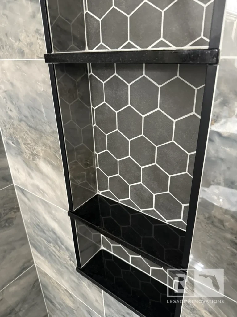 Recessed shower niche with black shelves and dark hexagon tile surrounded by gray wall tile in Jacksonville, FL