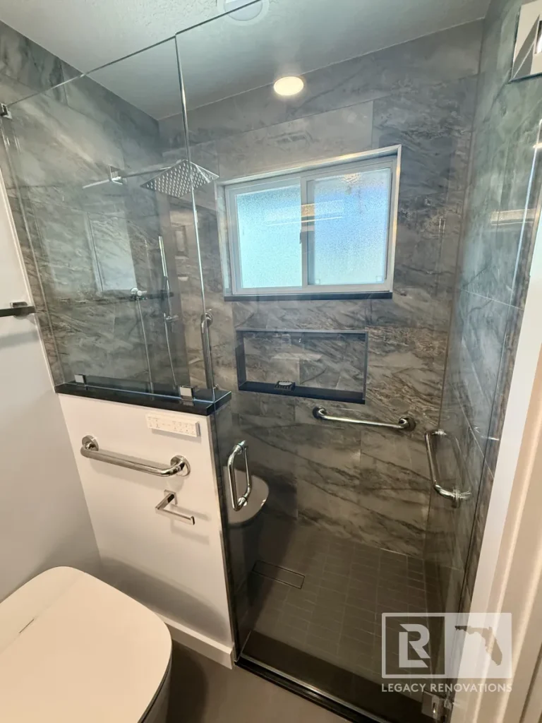 Tiled shower stall with square rain showerhead, frosted window, horizontal niche, grab bars, square tile floor, glass door, and adjacent toilet unit.