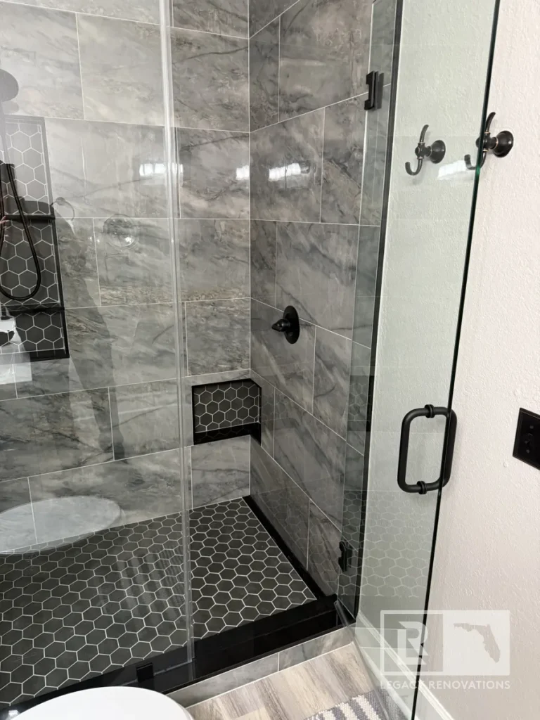 Glass shower enclosure with gray wall tile, black hexagon floor tile, recessed niche, and matte black fixtures in Jacksonville, FL