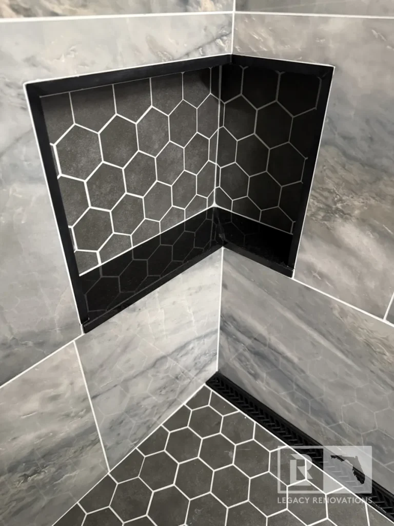 Recessed shower niche lined with dark hexagon tile and black trim above a matching hexagon tile floor in Jacksonville, FL