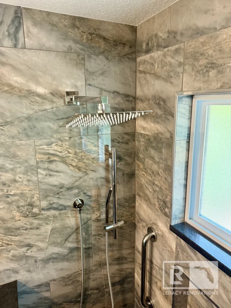 Wall-mounted chrome square rain showerhead over an adjustable slide bar wand fixture, flexible hose, curved grab bar, and frosted glass window.