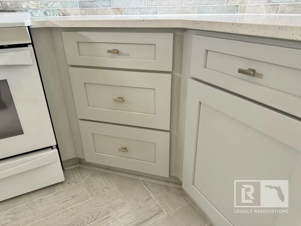 Three-tier grey drawer bank with horizontal metal knobs positioned next to a white oven range and engineered stone countertop.