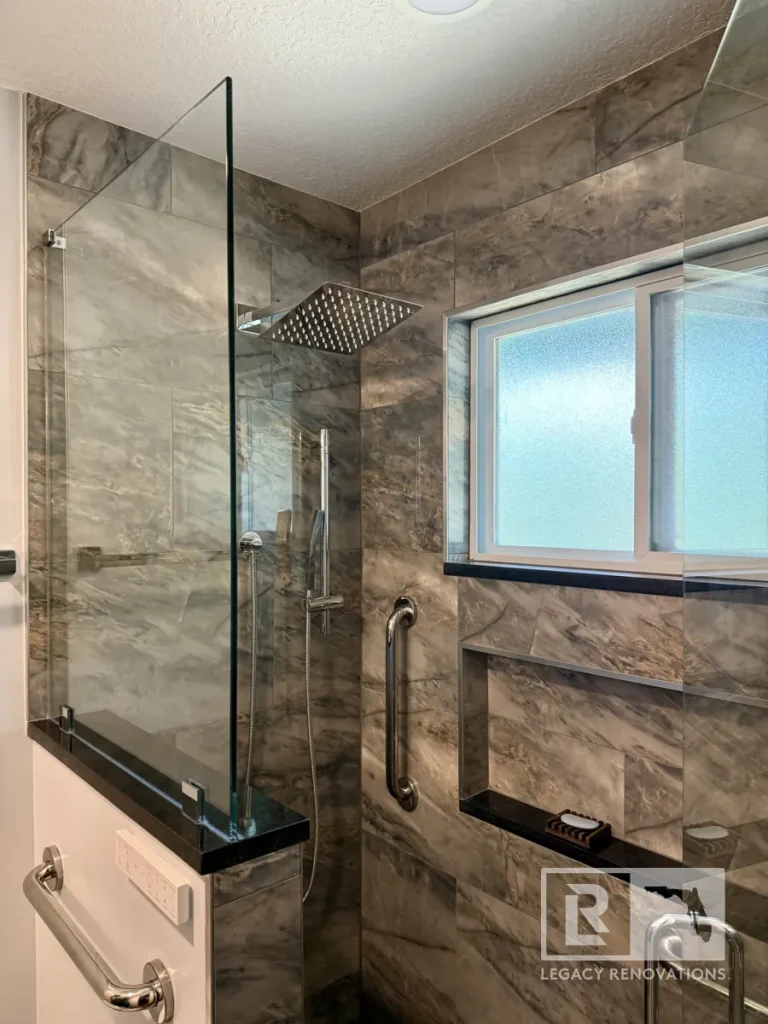 Angled shot of a tiled shower stall featuring a recessed horizontal wall niche with soap dish, square rain head, slide bar wand, frosted sliding window, and vertical safety grab bar.