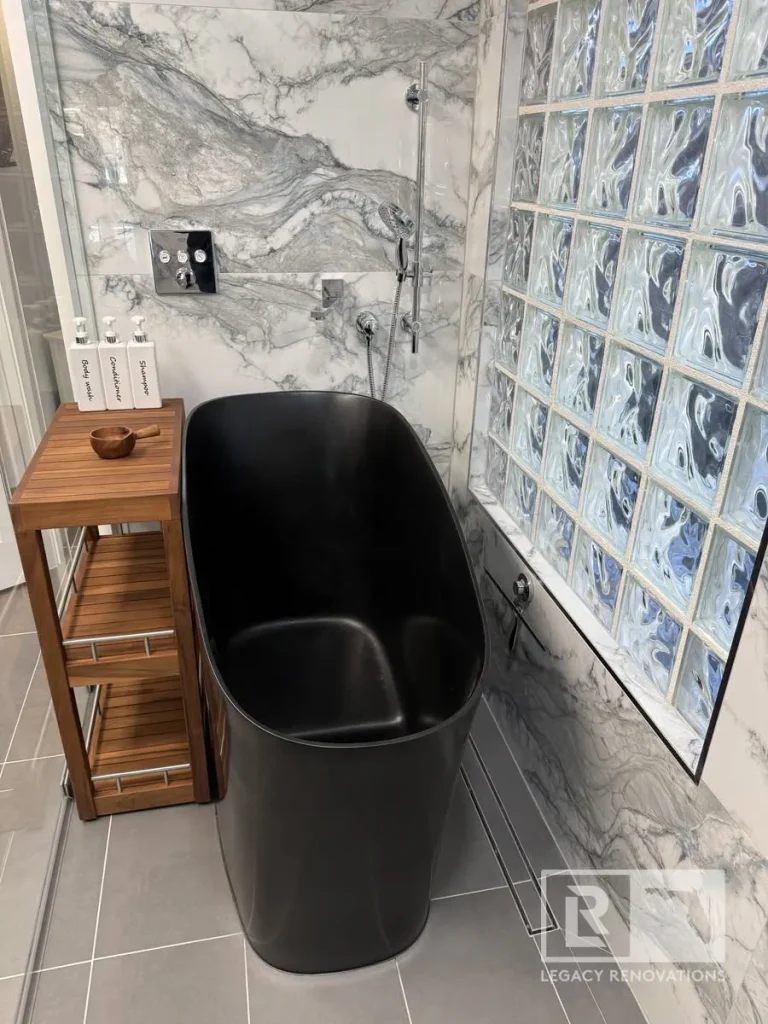 Black freestanding bathtub beside a glass block wall with gray veined shower surround in Jacksonville, FL