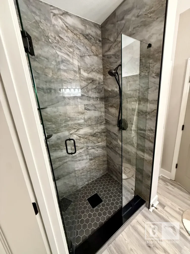 Glass shower enclosure with gray stone-look wall tile, black fixtures, and hexagon floor tile in Jacksonville, FL