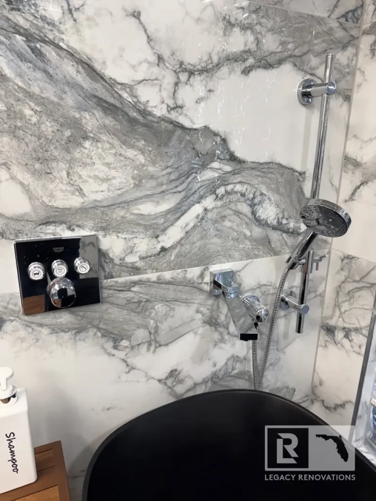 Gray and white veined shower wall with handheld showerhead, chrome controls, and tub edge in Jacksonville, FL