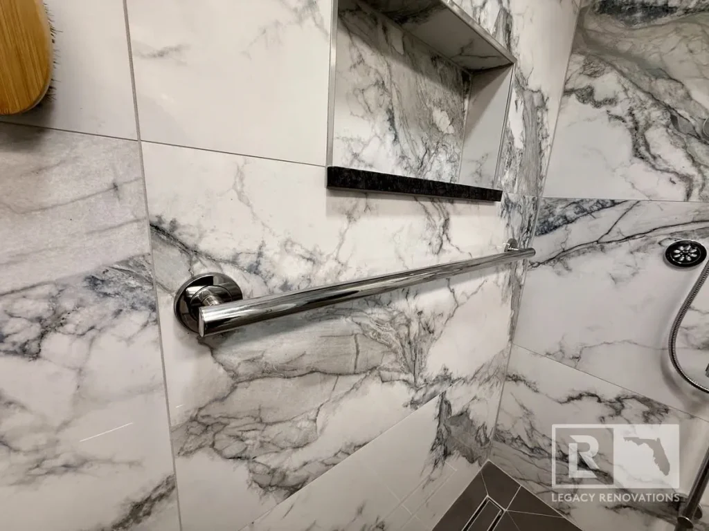 Accessible walk-in shower with marble-look porcelain tile, stainless steel grab bar, recessed shower niche, and body spray system in Jacksonville, FL.