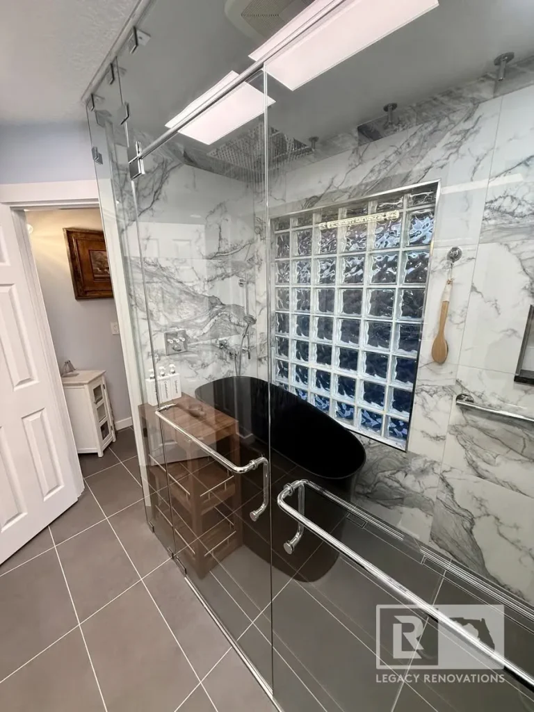 Jacksonville, FL bathroom remodel featuring a frameless glass shower, marble-look walls, glass block window, and black freestanding tub